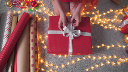 Girl creates New Years packages with red paper, colored ribbons. A young woman is packing Christmasの写真素材