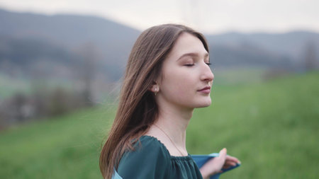 Beautiful brunette girl on the nature among the grass and flowers. She is walking in the middle