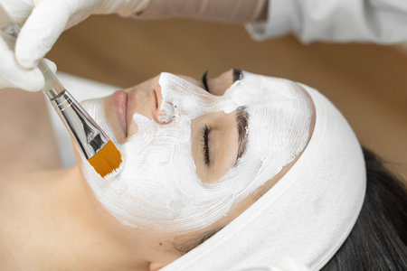 Professional touch: skills and professionalism of a cosmetologist who applies a cosmetic mask for facial skin care with tenderness and attention. A moment of relaxation and rest for the skin and mindの写真素材