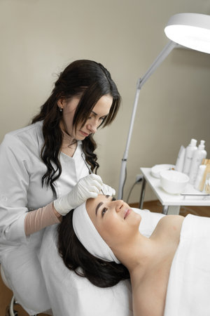 The photo reflects the therapeutic procedure of deep cleansing of the skin of the face, during which a beautiful woman finds harmony and relaxes in a beauty clinic. Cosmetologist works in the officeの写真素材
