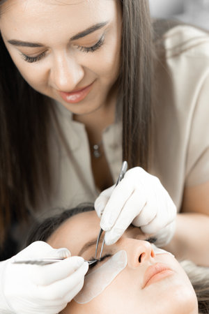 Photo shows moment when the beautician completes eyelash extensions by adding finishing touches to gorgeous look. Result is naturally attractive eyelashes that emphasize individuality and beauty womanの写真素材