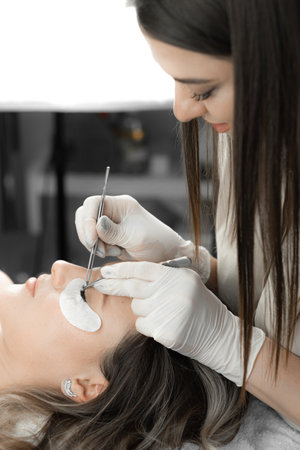 Woman lies relaxed, and lashmaker carefully builds eyelashes, creating wonderful decoration effect...