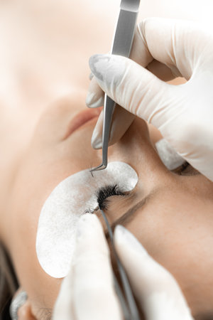 The photo offers you a look at the expert hand of a cosmetologist, who with proper technique extends eyelashes, giving expressiveness and attractiveness to the face. Top viewの写真素材