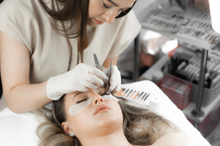 Photo that conveys atmosphere calm and relaxation in beauty salon during eyelash extension procedure. Beautician works with concentration, creating sophisticated look eyelashes.の写真素材