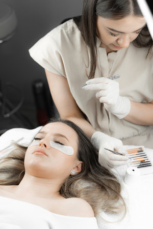 Take look at this fascinating photo, where beautician masterfully extends clients eyelashes, giving her expressive and elegant look. Beautician works in beauty salon, takes eyelashes with tweezersの写真素材