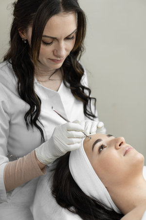 A young woman in a beauty salon enjoys a deep facial cleansing procedure that helps her relax and provide skin care. Professional osmetologist in beauty clinicの写真素材