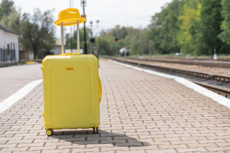 A yellow suitcase with a hat stands on a platform. Luggage before going on vacation. Suitcase for traveling and traveling on vacation.の写真素材