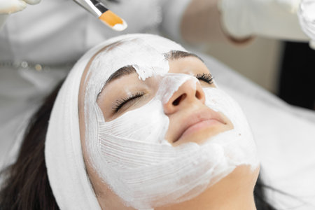 A woman is receiving a professional facial treatment at a spa, applying a white cream mask to rejuvenate her skin and achieve a radiant, youthful look. The atmosphere is tranquil and relaxingの写真素材