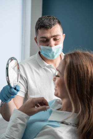 In a dental clinic, the patient rests in a chair, looks in the mirror at the result of work and dental treatment, relying on the experience and qualifications of the doctor who performs the treatment.の写真素材