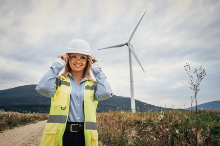A confident female engineer excels at a wind farm, demonstrating her engineering skills, dedication to sustainability, and strong leadership in a challenging outdoor construction settingの写真素材