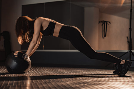 In a modern gym, a dedicated woman trains rigorously with a heavy medicine ball, demonstrating her...