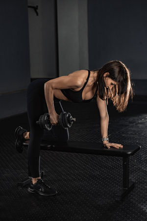 Focused Fitness A Woman Engaging in Strength Training with a Dumbbell at the Gym to Enhance Her Physical Wellbeing and Achieve Her Fitness Goals Through Effective Workout Routinesの写真素材