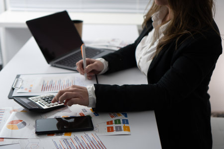 A skilled business professional analyzes data sets and financial reports from an organized desk, using a laptop to review documents with precision and meticulous attention to detailの写真素材