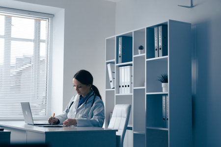 In a modern medical office, a skilled female doctor manages various documents and patient notes, demonstrating her expertise while maintaining a calm and organized environment that promotes wellnessの写真素材