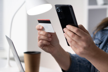 This image shows a closeup view of an individual holding a smartphone in one hand while gripping a credit card in the other, capturing the essence of modern transactions and consumer behaviorの写真素材