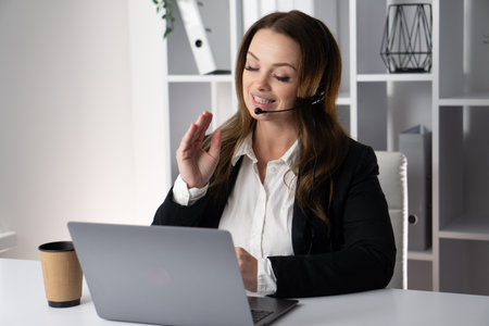 A confident businesswoman participates in a virtual meeting, showcasing professionalism and focus while discussing strategies with her team from her modern workspace using technologyの写真素材