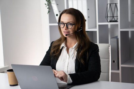 A professional woman is actively engaged in virtual communication while working at her modern office, demonstrating a strong focus and concentration on her client consultation and digital networkingの写真素材