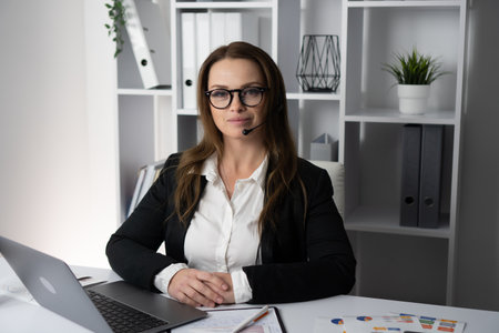 This image showcases a professional woman working diligently in an office setting while wearing a headset, representing traits such as confidence and motivation in her career and communication skillsの写真素材
