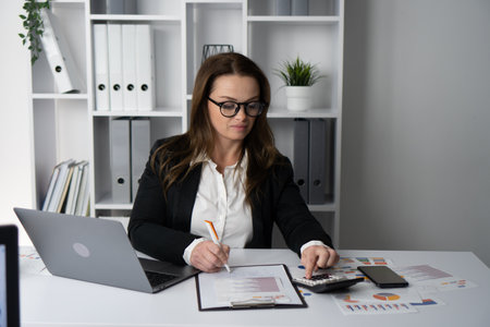 A focused businesswoman is deeply analyzing important data and information while situated in a contemporary office environment designed for maximum productivity and success in her corporate careerの写真素材