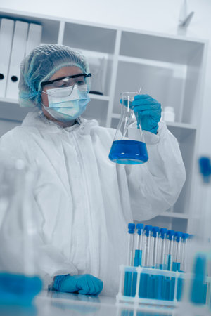 A scientist is meticulously conducting an experiment in a modern laboratory, carefully handling a flask filled with a vibrant blue liquid, ensuring accuracy and safety as part of the research processの写真素材