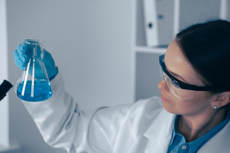A scientist in a lab is analyzing a blue solution for a research project, using advanced technology and precision equipment in chemistry and biotechnology to seek innovative healthcare solutionsの写真素材