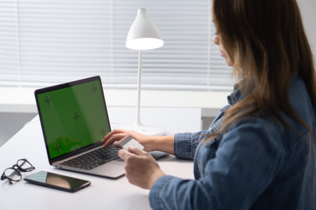 A woman works on a laptop at a bright, organized desk with modern decor, focused and comfortable. The inspiring lighting enhances her productive environment, merging technology and designの写真素材