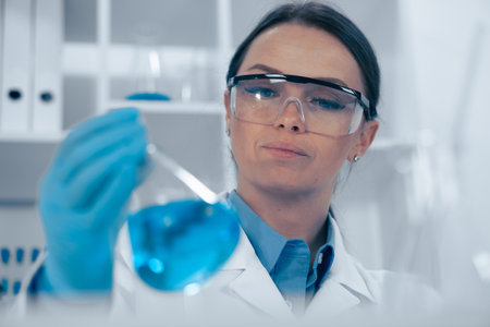 A female scientist is conducting an indepth analysis of a blue solution in her laboratory, showcasing her expertise in biochemistry and biotechnology through meticulous research and testingの写真素材