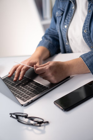 A CloseUp Image Capturing a Person Actively Typing on a Laptop While Having a Smartphone Placed Nearby, Illustrating Modern Communication and Digital Productivity in a Workspace Settingの写真素材