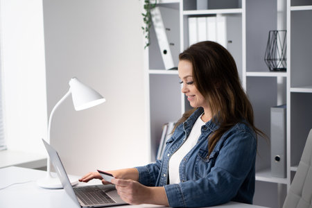 A woman is seen engaging in online shopping while working in a modern workspace, highlighting the blend of business and consumerism, showcasing the convenience of digital ecommerce todayの写真素材
