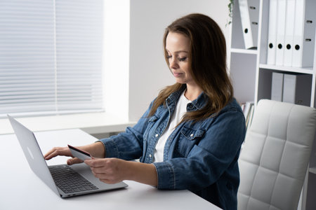 A woman is joyfully engaged in online shopping from her desk, comfortably using her laptop to explore a variety of products and make purchases, all from the cozy comfort of her own homeの写真素材