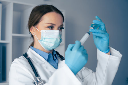 A dedicated healthcare professional is focused on preparing a vaccine injection with precise care and attention to detail in a clinical setting to ensure safety and effectiveness of the procedureの写真素材