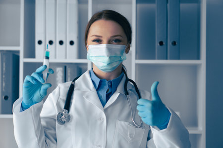 A confident healthcare professional in gloves and a mask holds a vaccine syringe with focus, demonstrating dedication to patient care and public health, while embodying trust in a clinical settingの写真素材