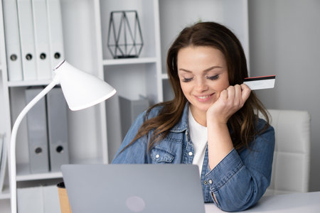 A thoughtful young woman deeply engaged in the activity of online shopping, showcasing the modern blend of convenience, enjoyment, and inspiration via her laptop in a trendy millennial lifestyleの写真素材