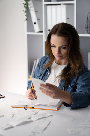 A focused young woman is deeply engaged in writing in a stylishly designed notebook while situated at a modern and aesthetically pleasing workspace that reflects her creative and organized lifestyleの写真素材