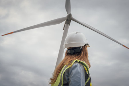 A confident female engineer in a hard hat and safety vest stands proudly before a wind turbine, highlighting her commitment to renewable energy and sustainability initiatives todayの写真素材
