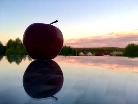 An apple lies on a glass table during a beautiful sunset and is reflected in it.の写真素材
