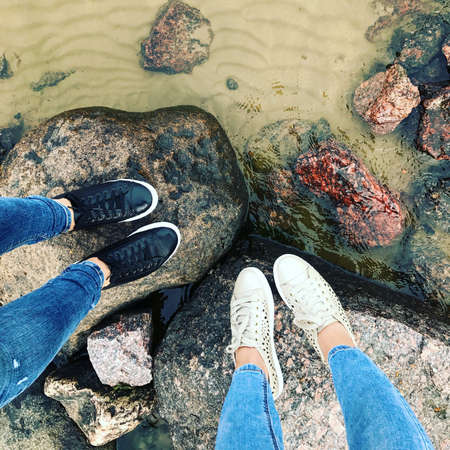 Legs in sneakers and jeans stand on stones in the water.の写真素材