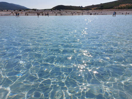 People walk in the shallow blue clear water of Lake