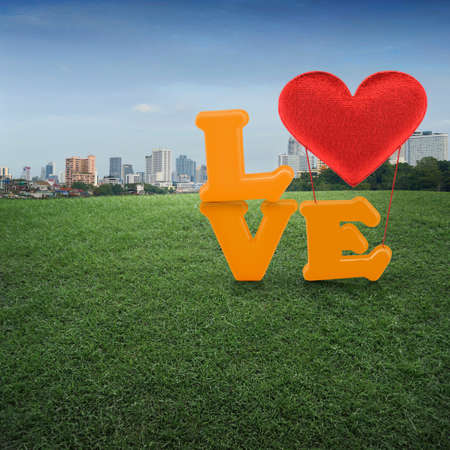 Love word with heart shape balloon on green grass field and office building city backgroundの写真素材