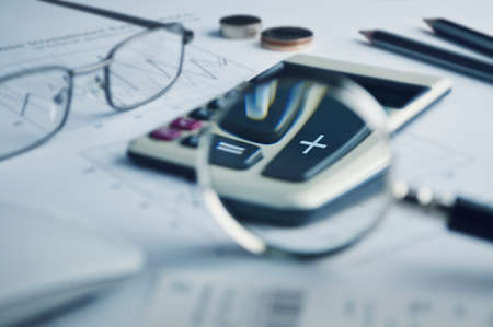 Calculator button plus and magnifying glass on graph paperの写真素材