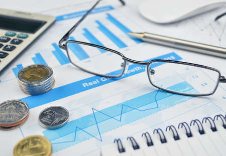 Glasses coin calculator and pen on financial chart and graph investment conceptの写真素材