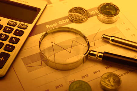 Magnifying glass, calculator, pen, and coin on financial graph, accounting background