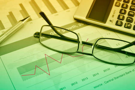 Glasses, pen and calculator on financial chart and graph, investment concept