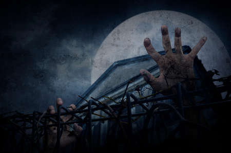 Hand over metal fence with dry leaves over old building and moon, Halloween conceptの写真素材