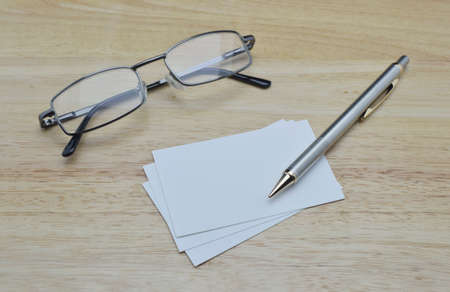 Blank business card with pencil and glasses on wooden office tableの写真素材