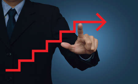 Businessman pointing to red arrow stair symbol on blue background, success conceptの写真素材