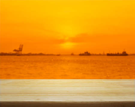 Empty wooden table over blur of cargo ship with shipping port at sunset sea, for your product...