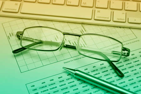 Glasses, pencil and keyboard on stock market graph, financial and business concept, green toneの写真素材