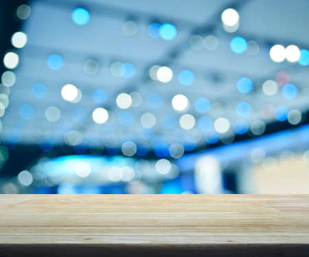 Empty wooden table over defocused light and shadow of shopping mall, blue tone