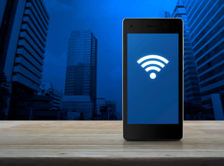 Wi-fi connection icon on modern smart phone screen on wooden table over city tower background,...